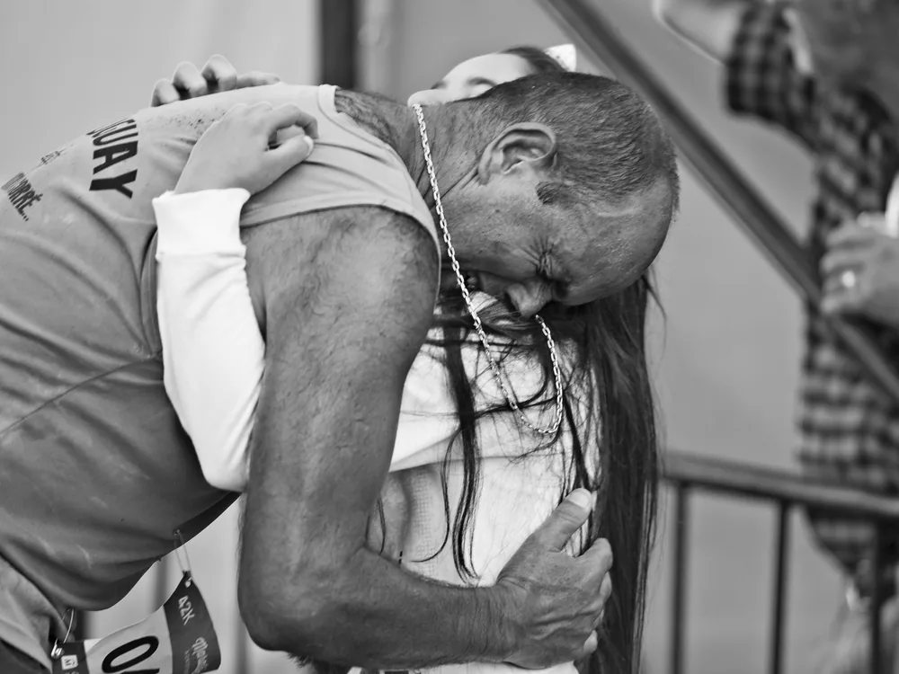 Abrazo emocionado entre un corredor y una niña en la llegada de una maratón, foto en blanco y negro de GeoDeportes