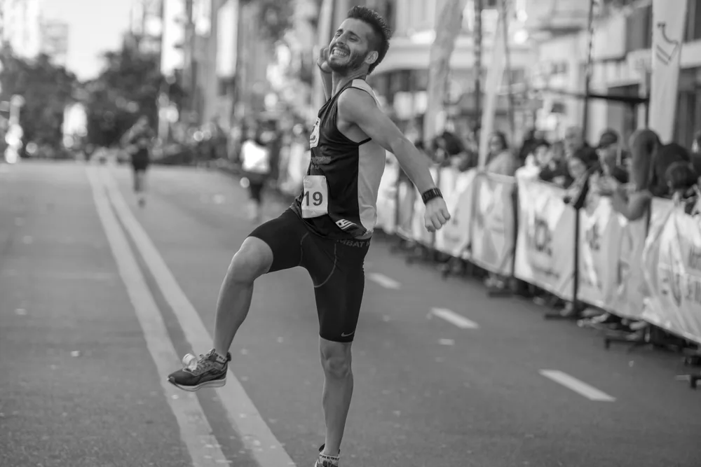 Corredor celebrando con una sonrisa al llegar a la meta de una carrera, foto en blanco y negro de GeoDeportes